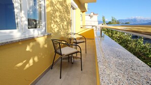 A balcony with two chairs and a table, overlooking a coastal road and mountains. - Appartement in Baška mit Eigenem Balkon by Interhome (Krk/Baška)