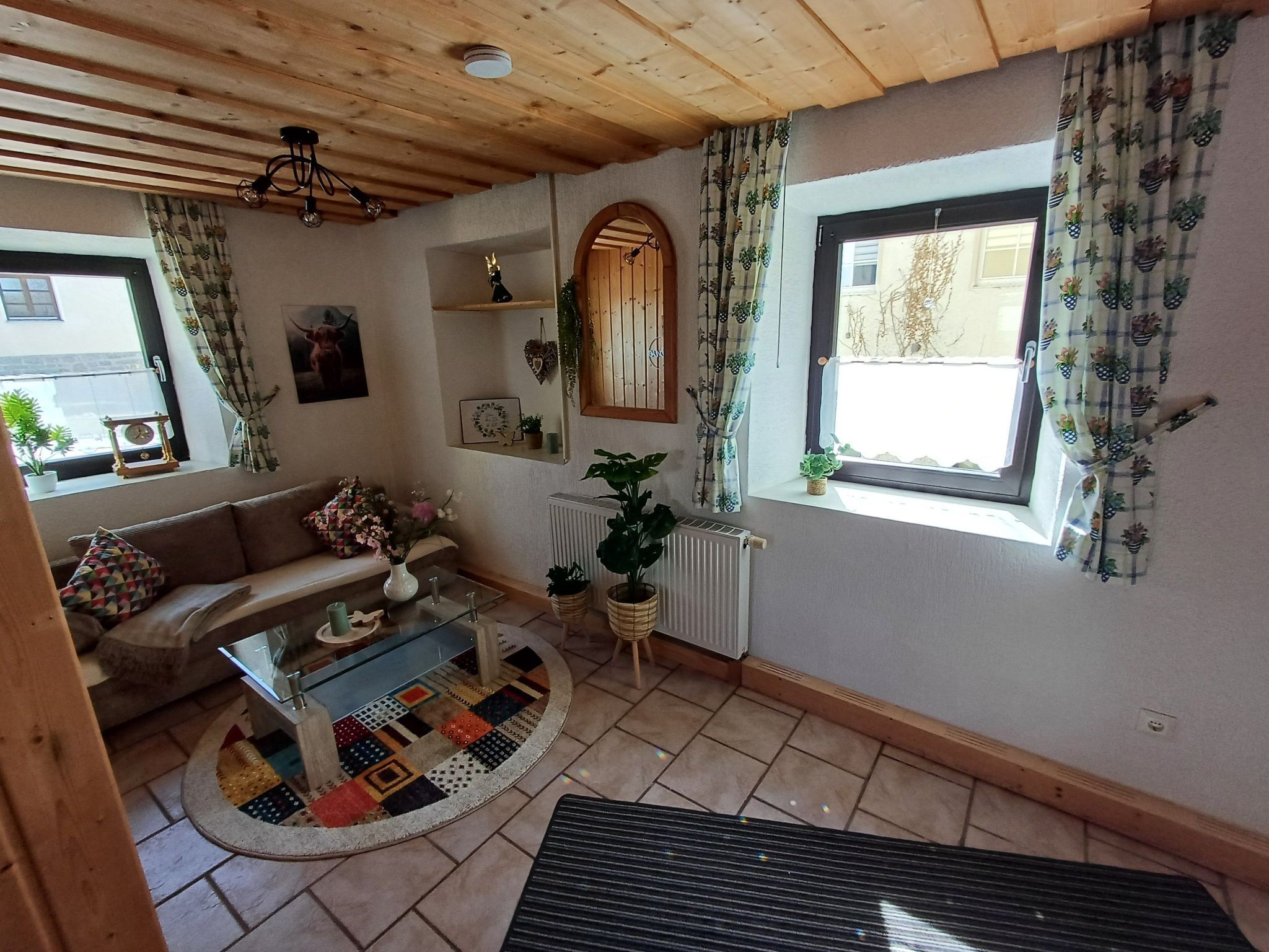 Un salon chaleureux avec un plafond en bois, un canapé, une table basse et une fenêtre avec des rideaux.