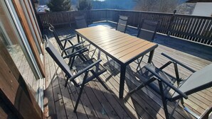 Terraza de madera con mesa y sillas, con vista a un área boscosa.