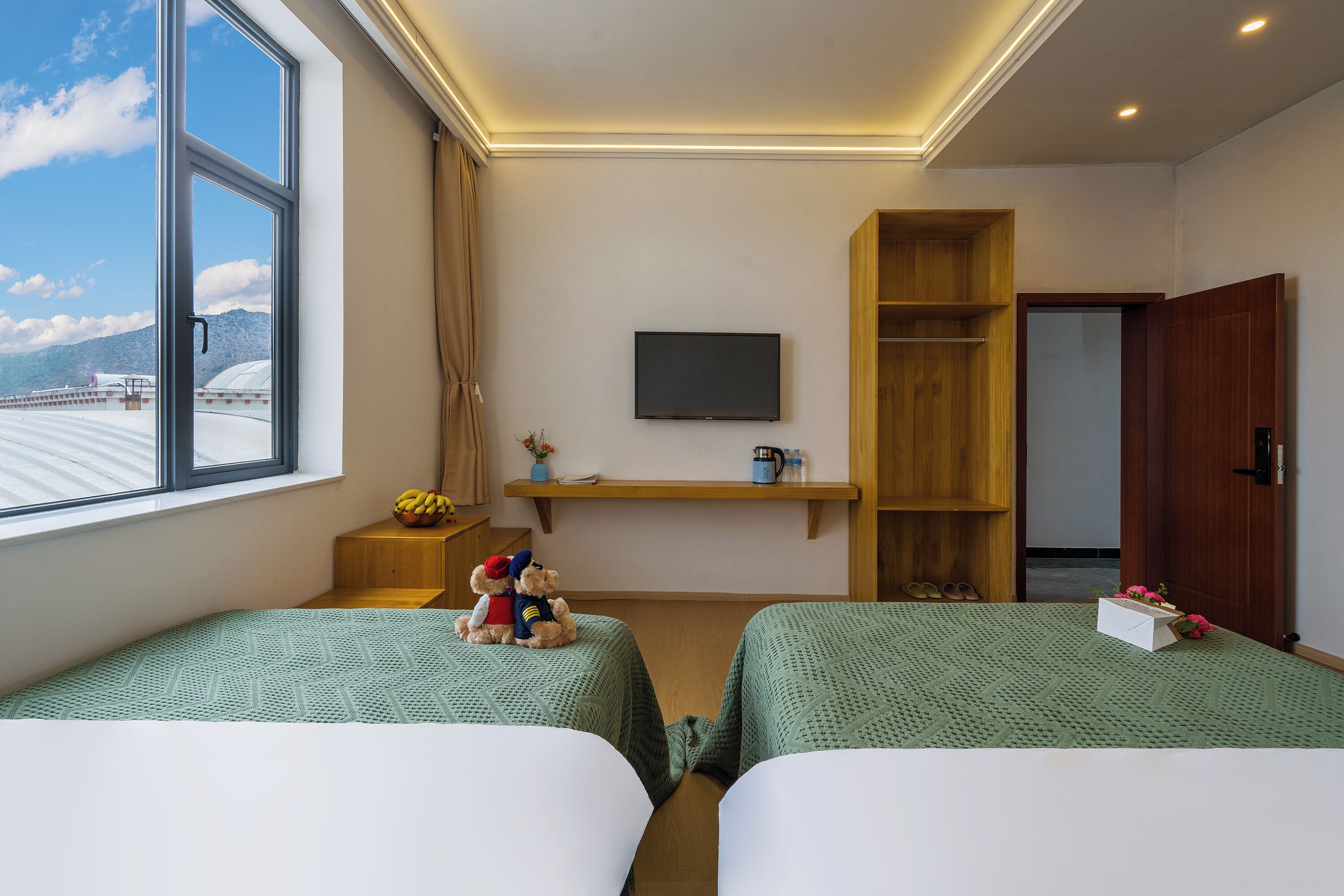 A hotel room with two beds, a TV, a wooden shelf, and a window with a view of mountains.