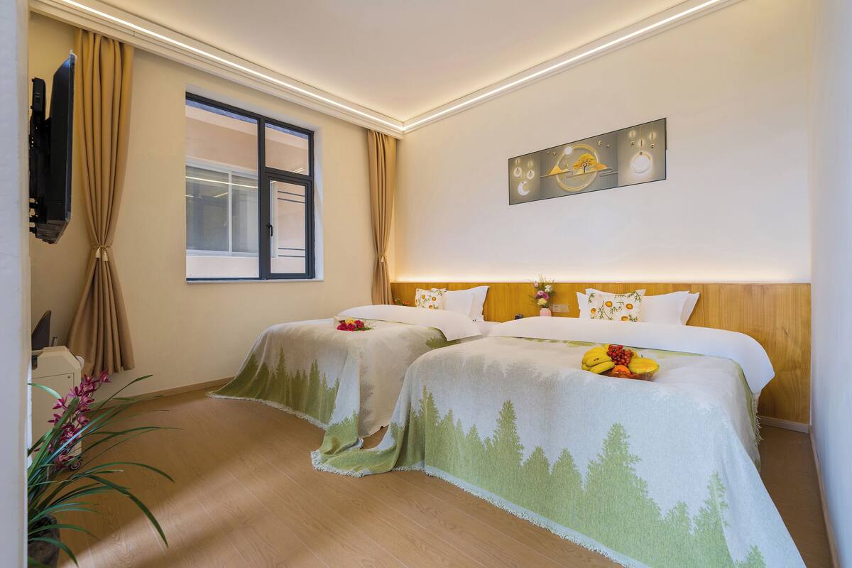 Een hotelkamer met twee bedden, een aan de muur bevestigde televisie en een raam met gordijnen.
