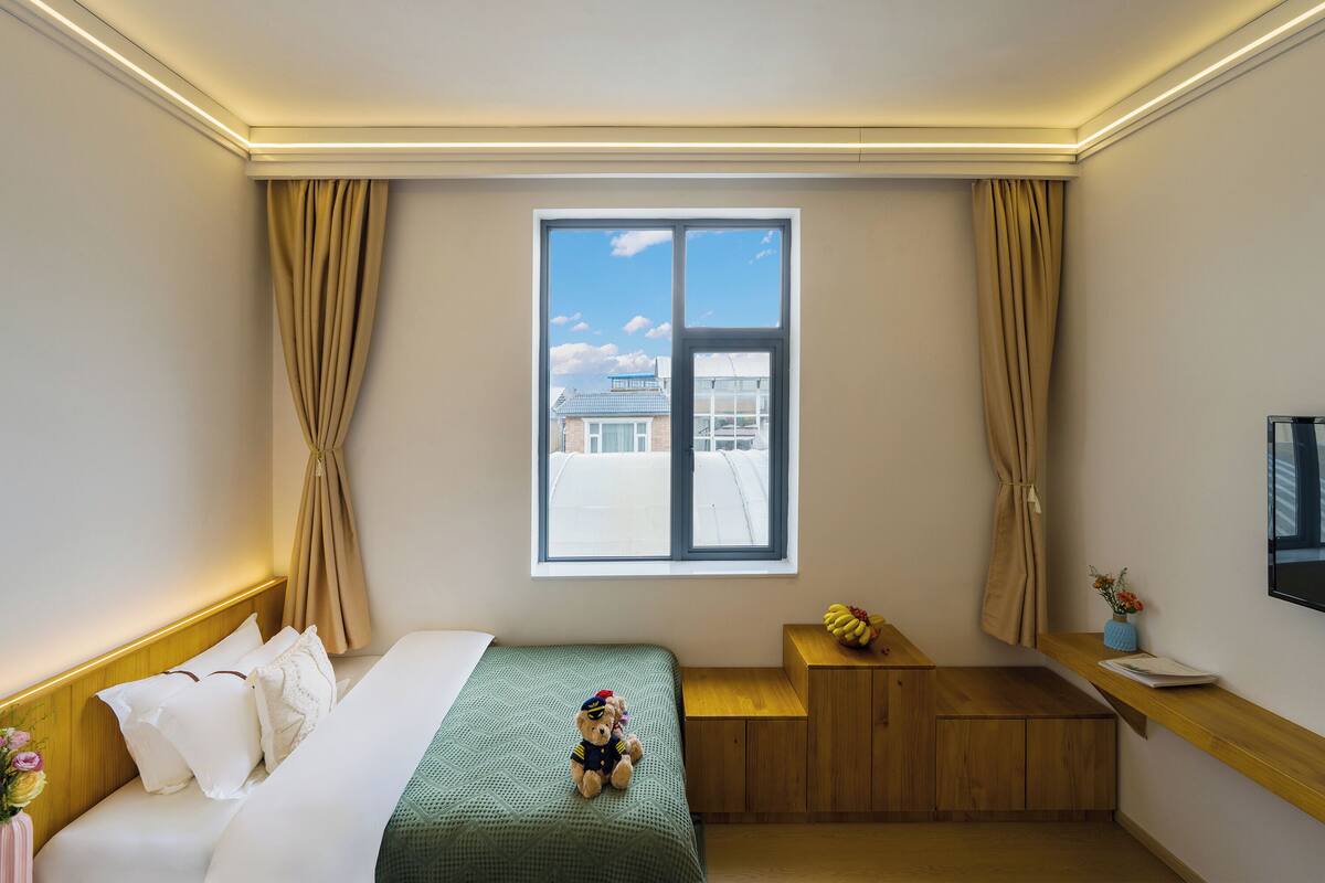 Een hotelkamer met een bed, een bureau, een raam met gordijnen en uitzicht op gebouwen.