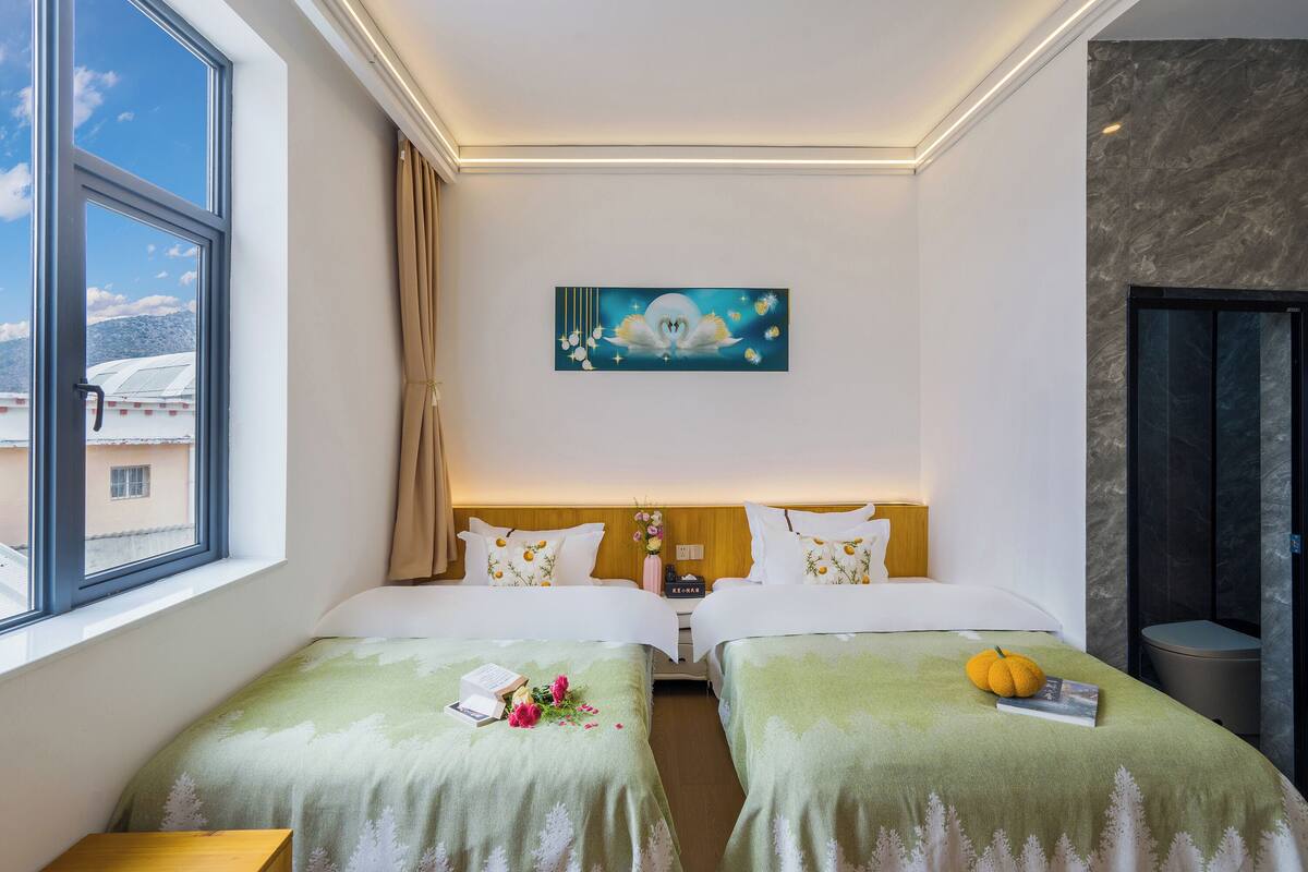 Een hotelkamer met twee bedden, een schilderij aan de muur, een raam en uitzicht op gebouwen.