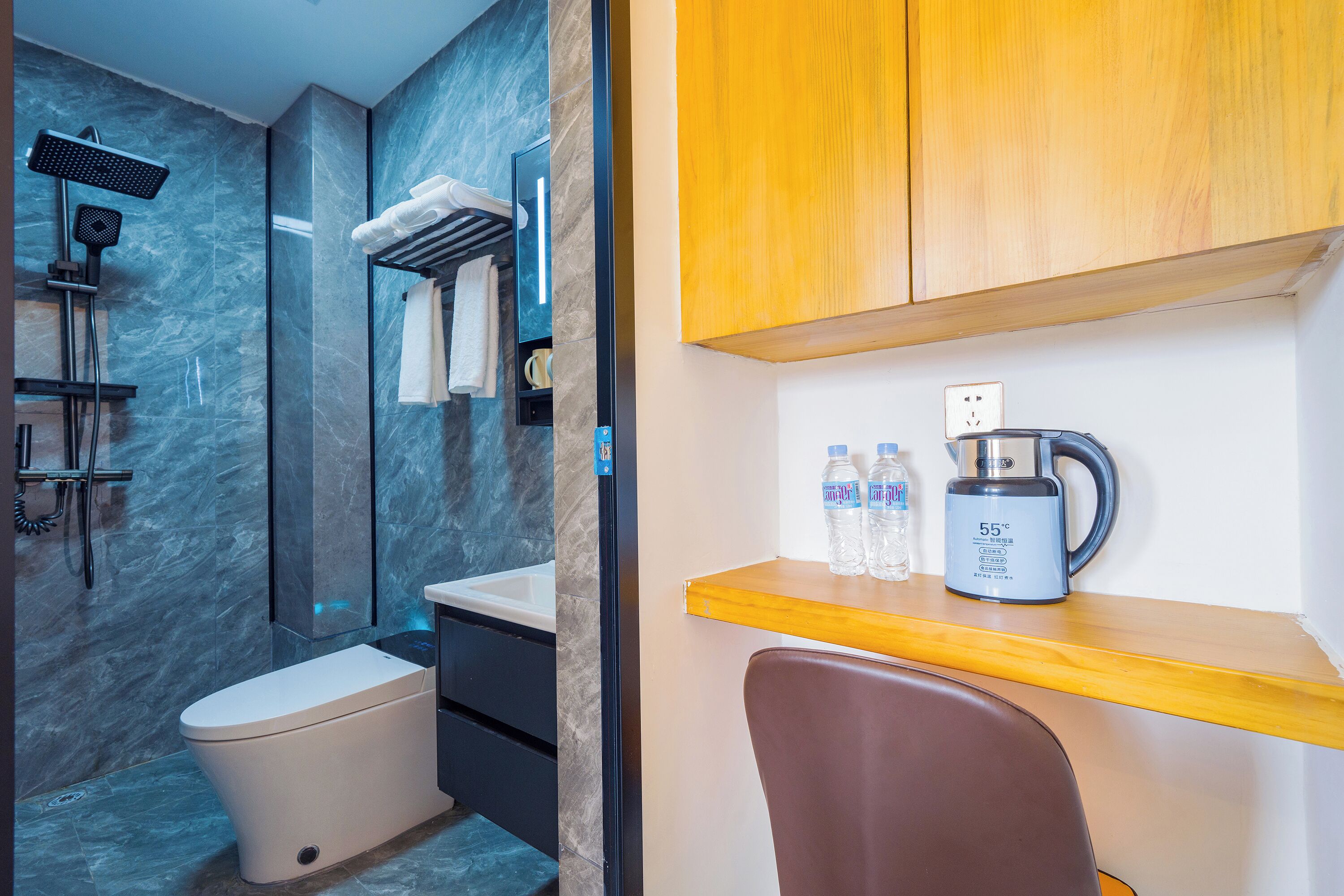 A modern bathroom with a shower, toilet, and a sink. There is a wooden shelf with a kettle and water bottles.