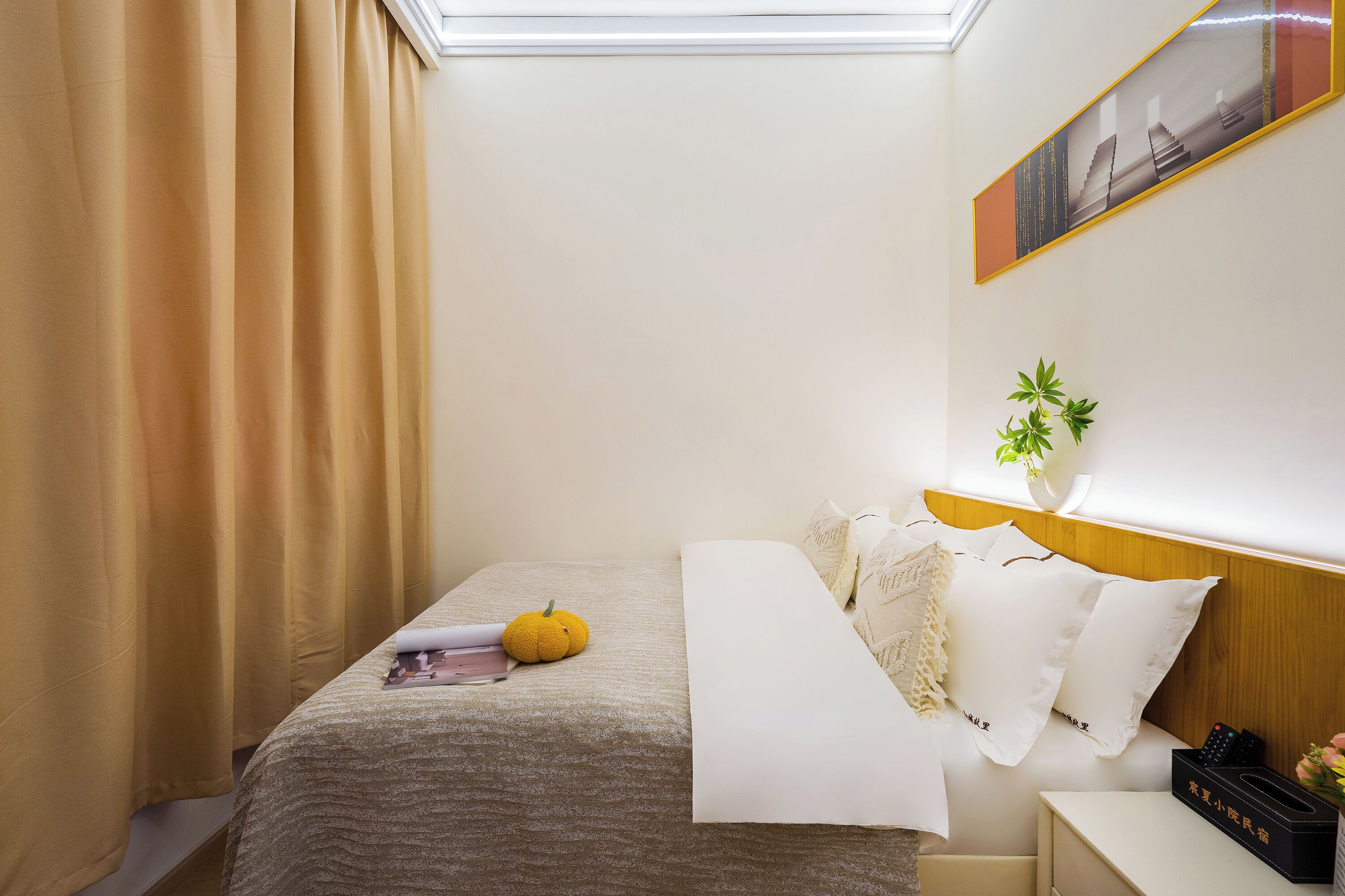 Un letto rifatto con cura, un comodino con un vaso di fiori e un quadro appeso al muro.