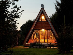 Uma cabana de madeira triangular com antena parabólica, janelas amplas e um pequeno alpendre.