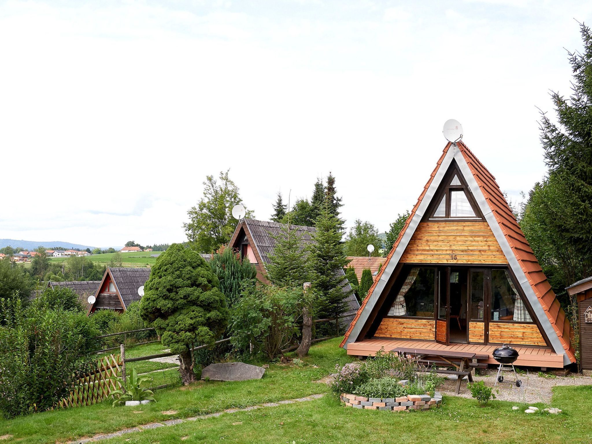 Une maison moderne de style « A », dotée d’une grande porte vitrée, entourée d’un jardin bien entretenu et d’une terrasse en bois.