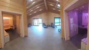 Un interior espacioso con techo alto, paredes de madera y una zona central de estar con sillas y una mesa.
