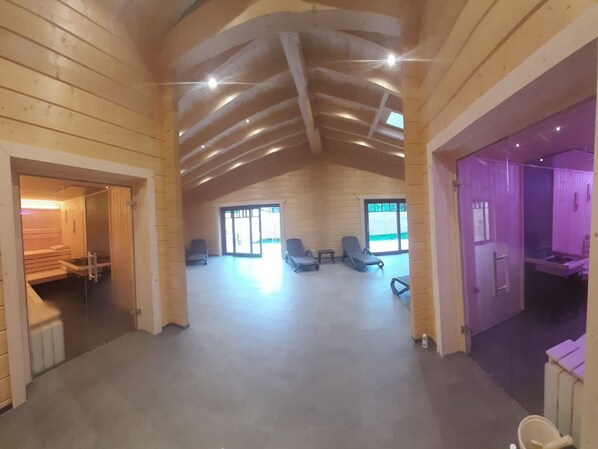Un interior espacioso con techo alto, paredes de madera y una zona central de estar con sillas y una mesa.