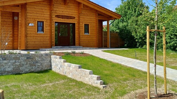 Una cabaña de madera con un muro de contención de piedra y un camino de entrada pavimentado.