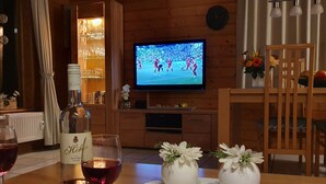 Un salón acogedor con un televisor mostrando un evento deportivo, una botella de vino y dos jarrones con flores sobre una mesa.