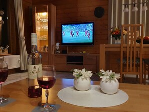 Un salón acogedor con un televisor mostrando un evento deportivo, una botella de vino y dos jarrones con flores sobre una mesa.