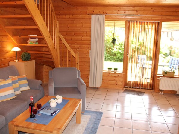 En inredning med trädetaljer, en soffa, en fåtölj och ett bord med en flaska och glas.