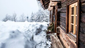 Eine Holzhütte mit verschneiter Fassade, einer Holzterrasse und einem Fenster mit Holzrahmen.