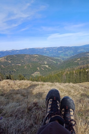 Une personne assise sur une colline herbeuse, d’où l’on peut admirer un paysage montagneux.