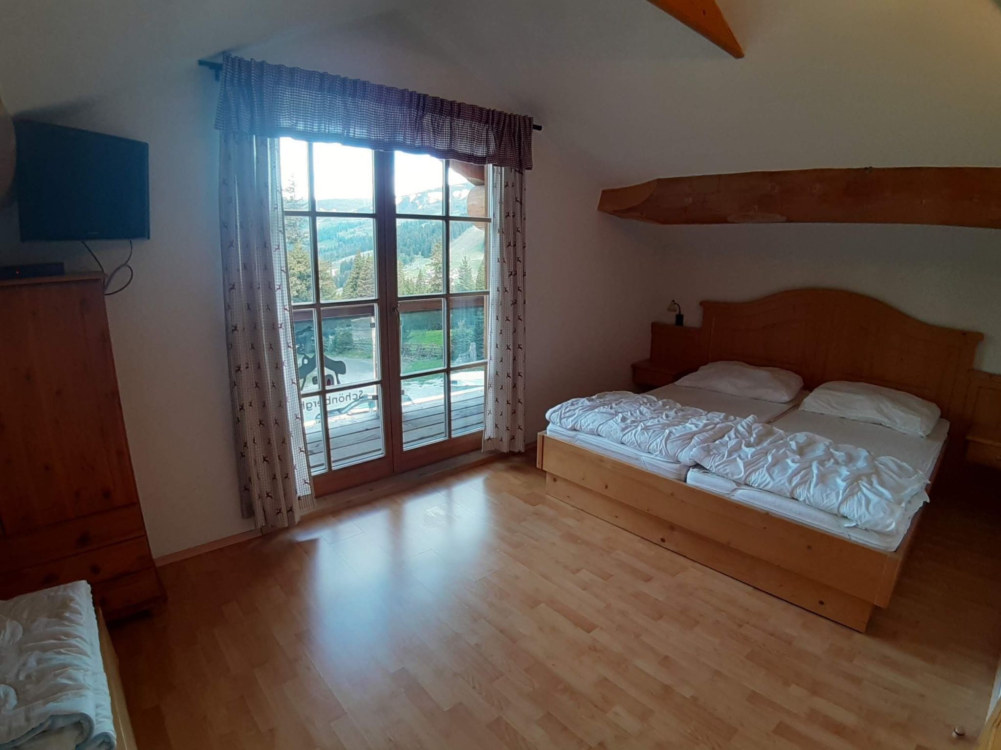 A bedroom with a large window, wooden floor, and a bed with white bedding.