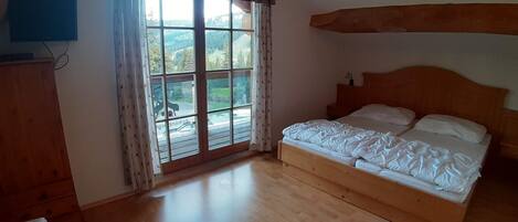 A bedroom with a large window, wooden floor, and a bed with white bedding.