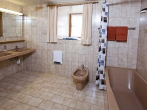 Un bagno con due lavandini, un bidet, una vasca da bagno e una finestra con tende.