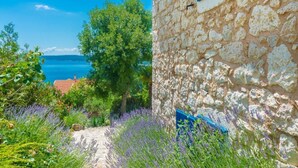 Un edificio in pietra con persiana blu, circondato da campi di lavanda e vista sul mare.