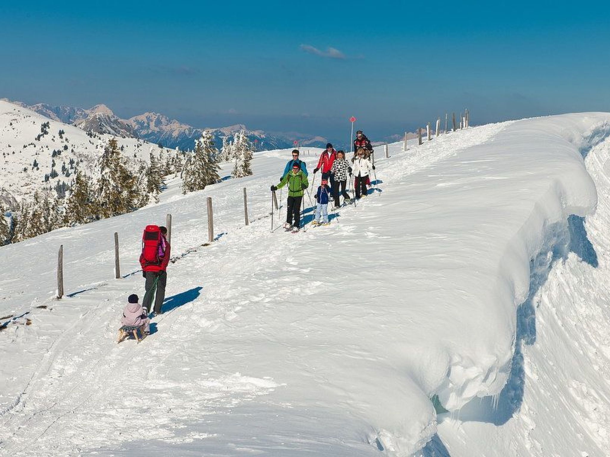 Encosta coberta de neve com esquiadores e um veículo vermelho.