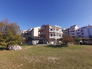 Ein mehrstöckiges Wohngebäude mit Balkonen, einer Steinmauer und einem Rasen mit Bäumen.