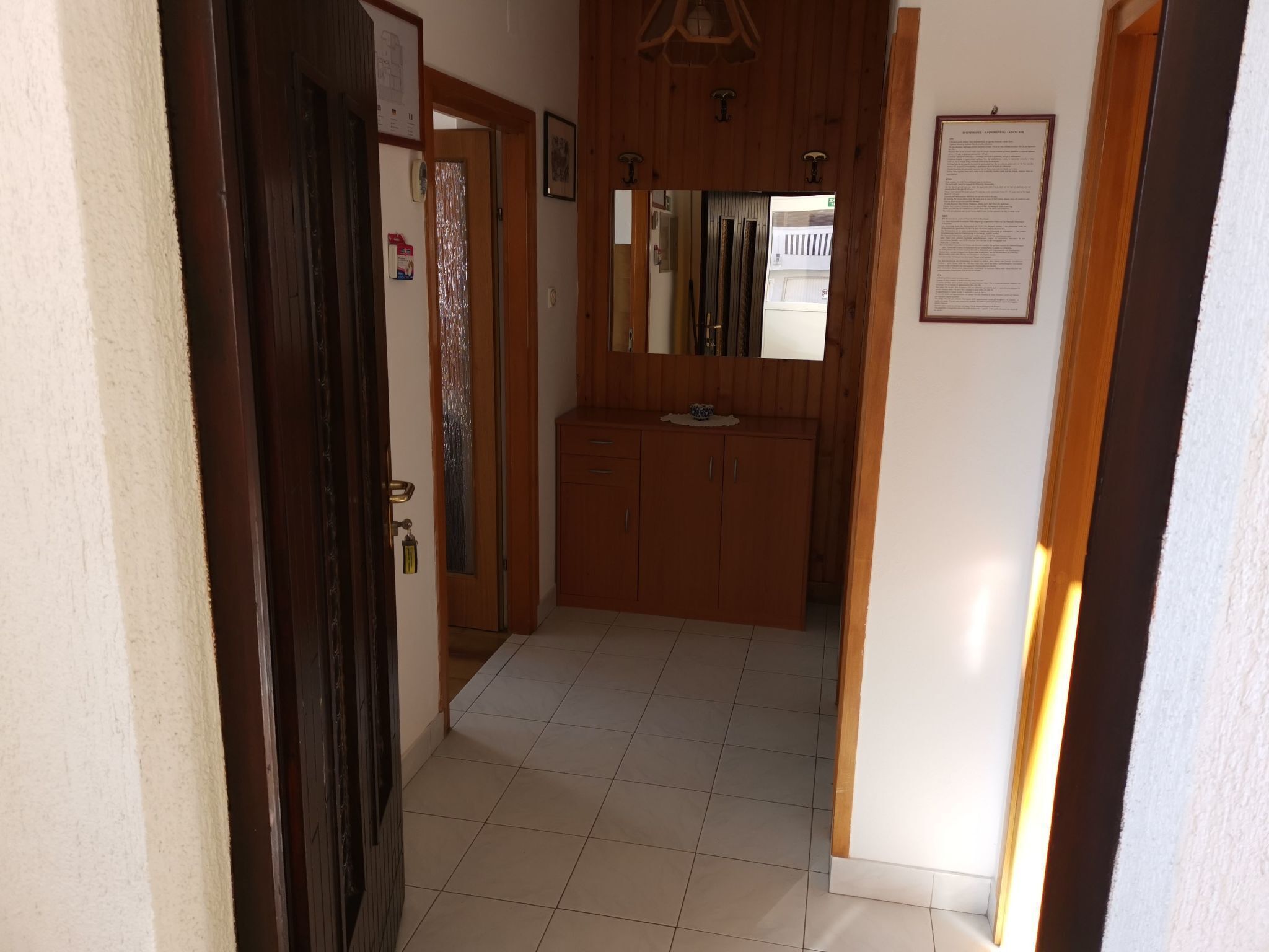 A hallway with a wooden door, a mirror, and a framed document on the wall.