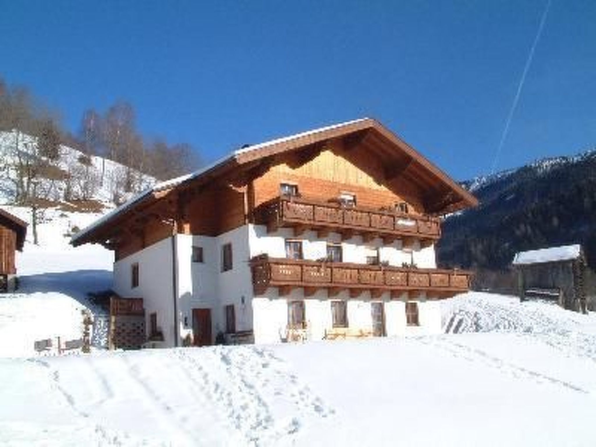 Una cabaña de dos plantas con balcón de madera, rodeada de nieve y montañas.