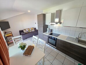 Eine moderne Küche mit Einbauofen, ein Essbereich mit weißem Tisch und Stühlen sowie ein graues Sofa mit floralen Kissen.
