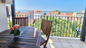 En balkon med et træbord og stole, en potteplante og udsigt over en kystby.