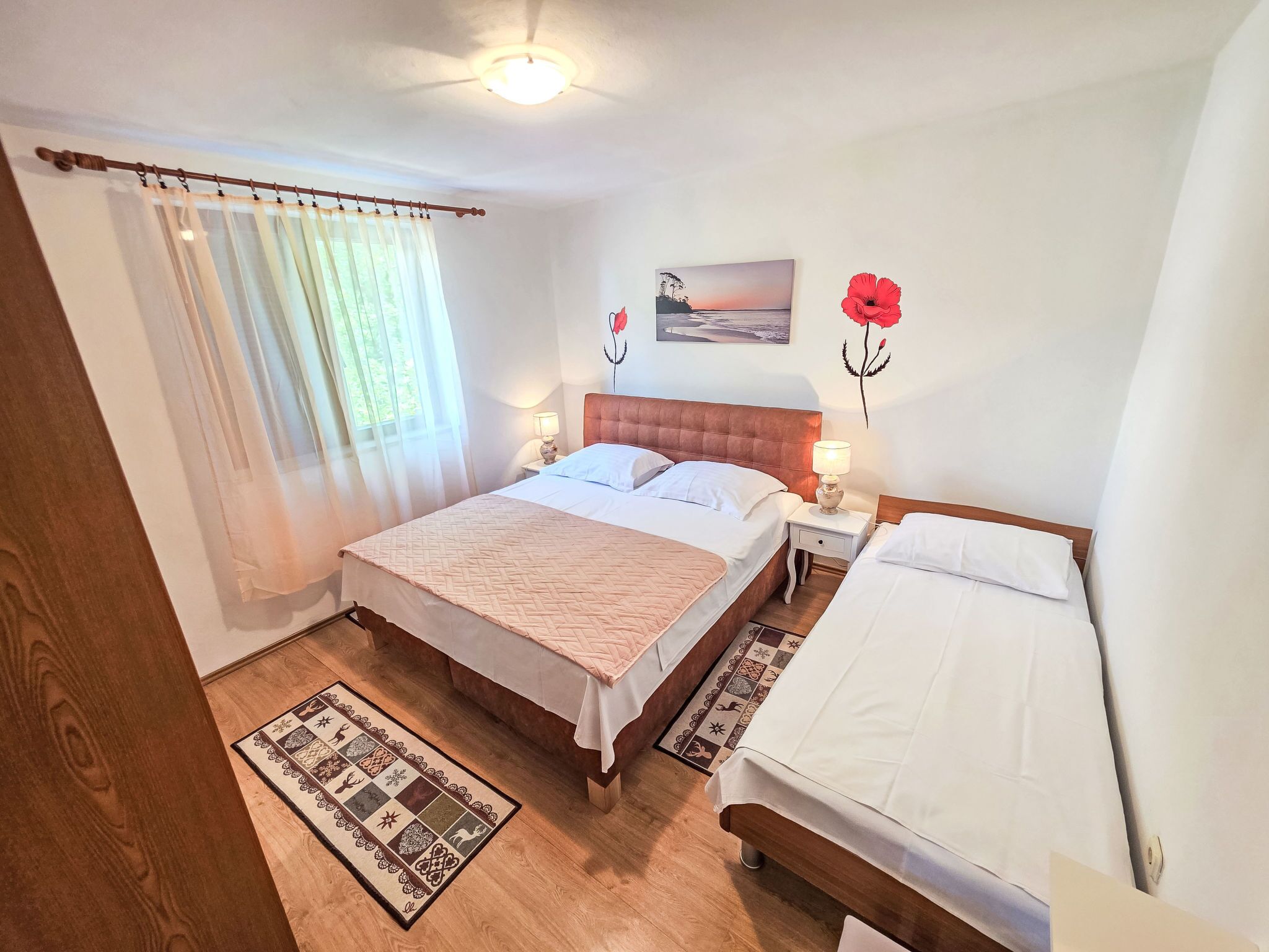 Ein Schlafzimmer mit zwei Betten, einem Nachttisch mit Lampe, einem Gemälde und einer roten Blumendekoration.