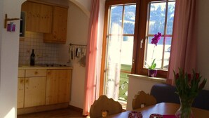 A kitchen with wooden cabinets, a dining table with two chairs, and a window with a view of mountains. - Gsenger in Abtenau by Interhome (Abtenau)