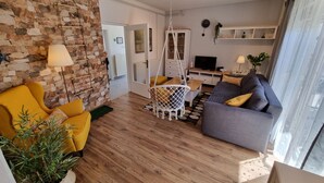 Ein Wohnzimmer mit Steinwand, Holzboden, einer Couch, einem gelben Sessel, einem Hängekorbstuhl und einem Fernseher.