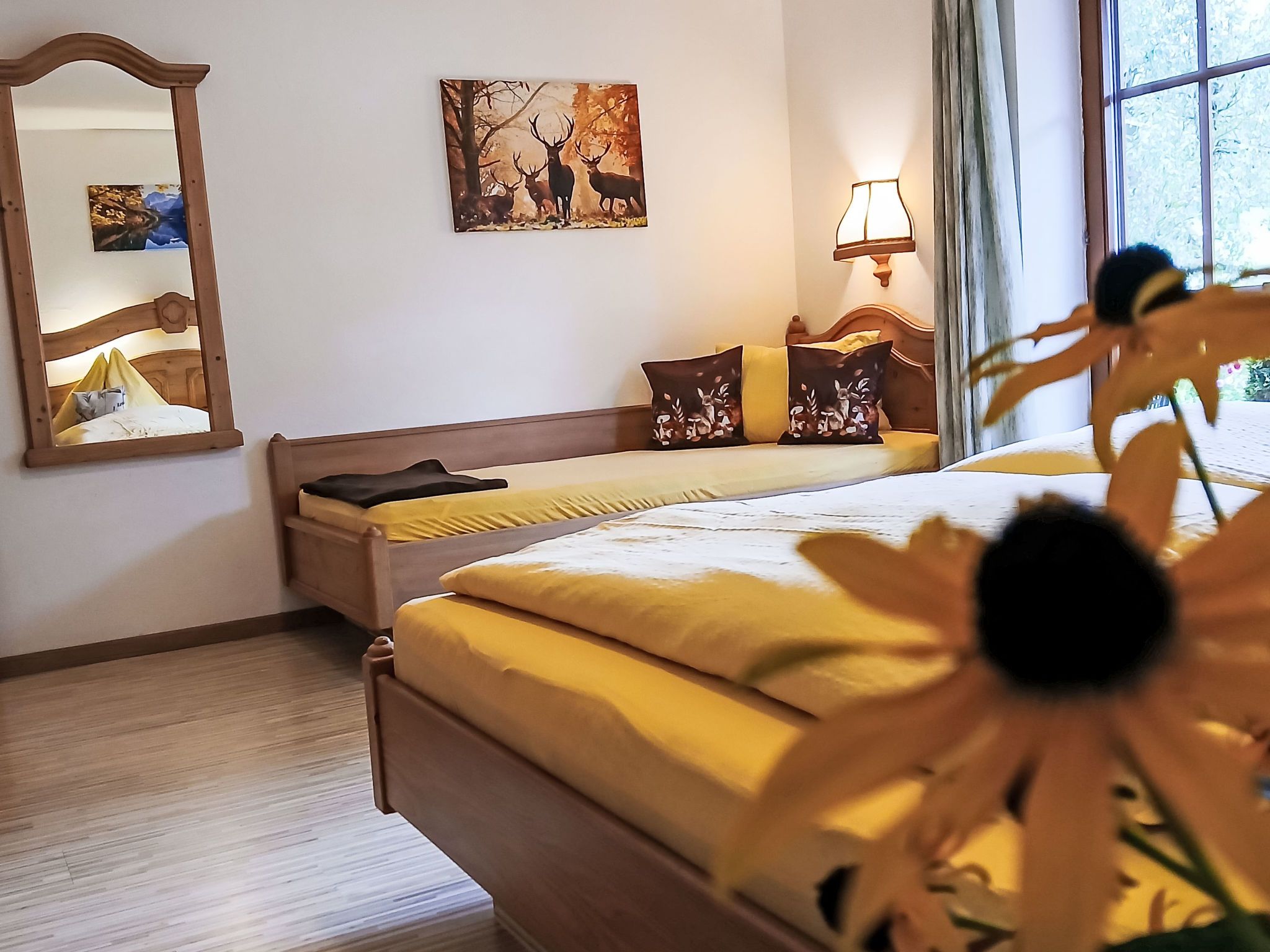 A hotel room with a bed, a mirror, a painting, a lamp, and a window.
