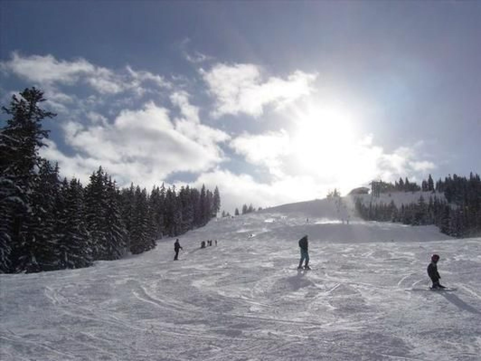 Une piste de ski enneigée, avec des skieurs et un ciel dégagé.