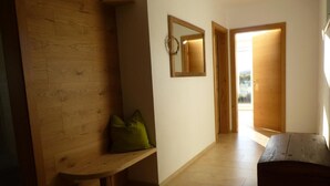 Un pasillo con un banco de madera, un cojín verde, un espejo y un cofre de madera.