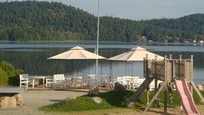 Um deck à beira do lago com área de estar ao ar livre, guarda-sóis e um parquinho.