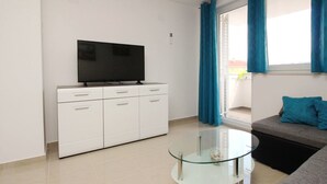 A modern living room with a flat-screen TV on a white cabinet, a glass coffee table, and a grey sofa with blue cushions. - Wohnung in Baška mit Eigenem Balkon by Interhome (Krk/Baška)