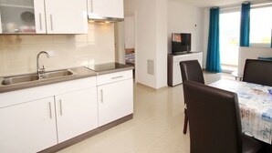 A modern kitchen with white cabinets, a stainless steel sink, and a built-in stove. There is a dining area with a table and chairs, and a TV on a stand. - Wohnung in Baška mit Eigenem Balkon by Interhome (Krk/Baška)