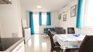 A modern kitchen with a built-in stove, a dining area with a table and chairs, and a sofa in the background. - Wohnung in Baška mit Eigenem Balkon by Interhome (Krk/Baška)
