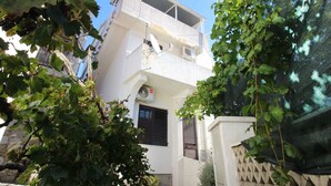 Un edificio de dos pisos con un balcón, una antena parabólica y un ventanal con contraventanas.