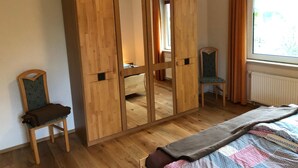 A bedroom with a wooden wardrobe, a single bed, a chair, and a window with curtains. - Haus am Reithmoor by Interhome (Großefehn)