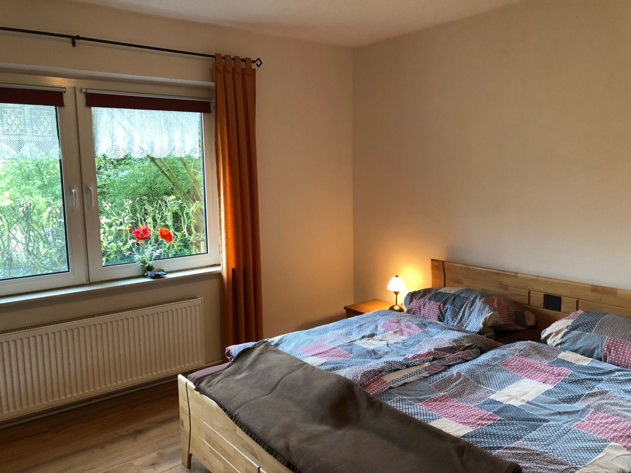 A bedroom with two beds, a window with curtains, a radiator, and a bedside lamp.