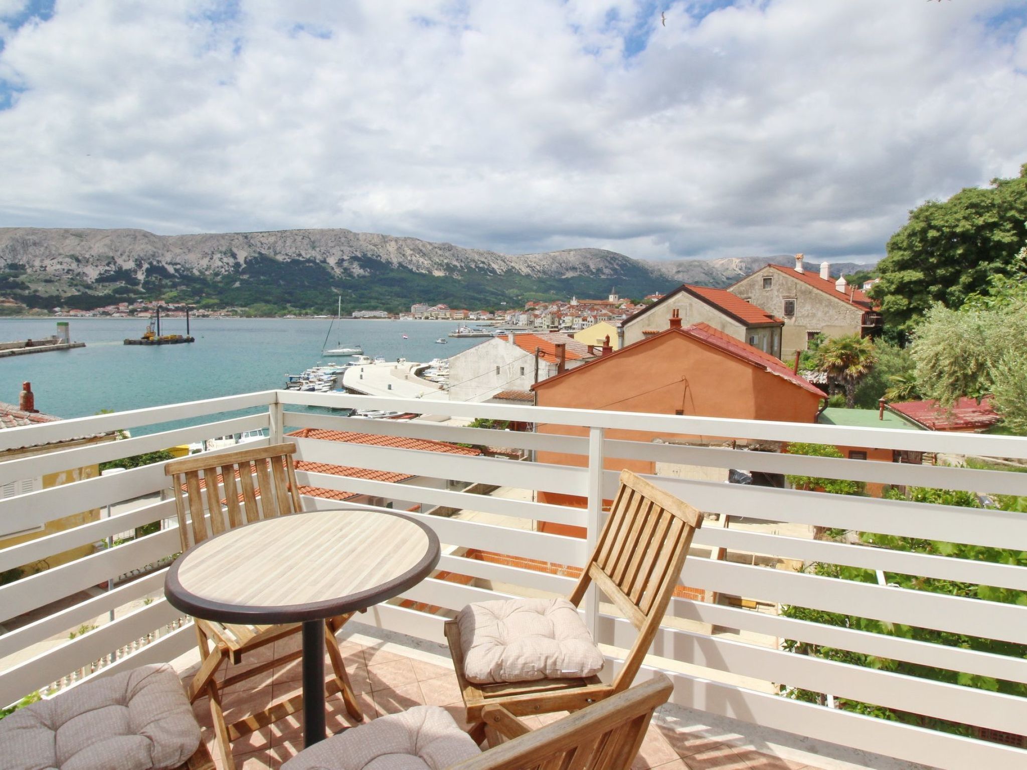 Un balcon avec une table et des chaises donnant sur une marina où sont amarrés des bateaux, ainsi que sur une ville côtière.