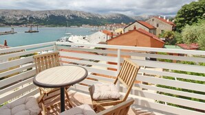 A balcony with a table and chairs overlooking a marina with boats and a coastal town. - C. Silvija Bs by Interhome (Krk/Baška)