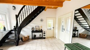 Un'ampia stanza con una scala, una panca verde e un piccolo tavolo con oggetti decorativi.