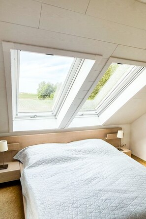 Une chambre avec un plafond en pente et des fenêtres de toit, un lit avec un matelas matelassé, des tables de chevet et une lampe.