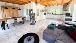 Un'ampia zona giorno con soffitto in legno, un tavolo da pranzo con sedie, un divano e una cucina con pensili bianchi e un piano cottura.