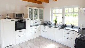 Una cucina moderna con mobili bianchi, forno integrato, microonde e macchina del caffè. Si vede una finestra con vista su spazi verdi.