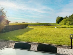 Une pelouse bien entretenue, agrémentée d’une haie, d’un petit bâtiment et d’un espace dallé avec des meubles en osier.
