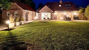Una casa a due piani in mattoni con un patio ben illuminato, un'area salotto esterna coperta e un prato.
